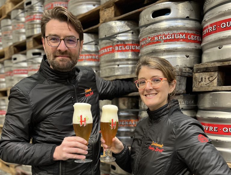 Paul & Céline Lefebvre (frère et soeur de la 6ème génération de la Brasserie Lefebvre) pose devant des fûts de bières, un verre de bière Hopus à la main.