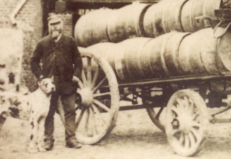 Jules Lefebvre (1ère génération et créateur de la Brasserie Lefebvre) pose à côté d'une charrette en bois portant des fûts en bois.