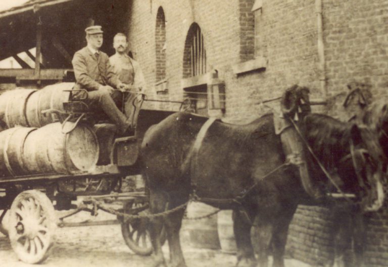 Jules et Auguste posent assis sur une charrette transportant des fûts de bières en bois et tirée par 2 chevaux. 